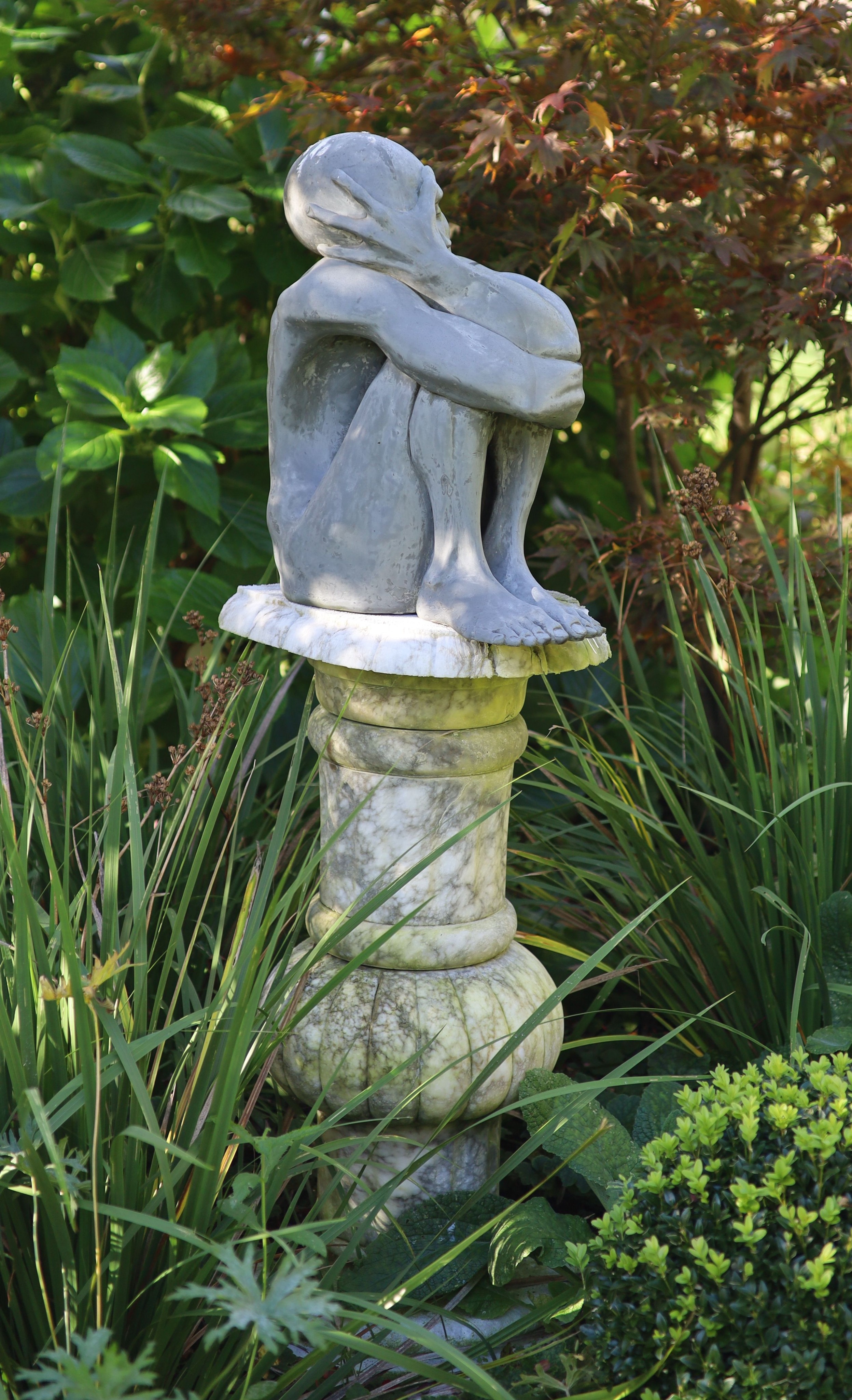 A simulated lead resin garden statue of a seated man, height 49cm, with a damaged marble pedestal, height 78cm